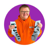 Man with down syndrome in orange hoodie holds up socks in each hand in pale grey with a crocodile pattern